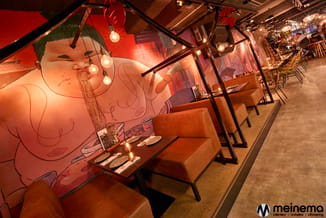Restaurantruimte met cognackleurige hoekbanken, zwarte tafels, hangende bolverlichting en grote rode muurschildering met abst