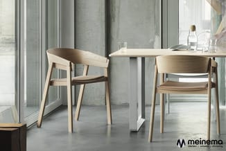 Lichte houten stoelen met bruine zitting aan witte tafel in moderne kantoorruimte met betonnen wand en grote ramen.