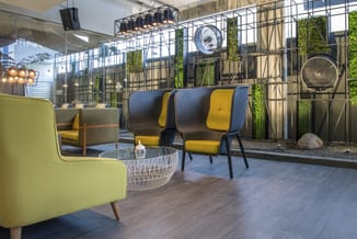 Modern kantoorlounge met gele fauteuil, blauwe en gele stoelen, witte bijzettafel, zwart metalen scheidingswanden en groene k