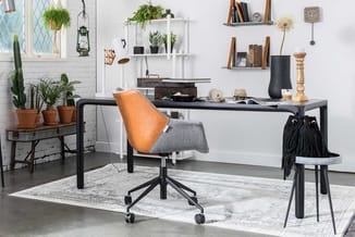 Kantoor werkplek met zwart bureau, oranje-grijze bureaustoel, potplanten, wandplanken, klok en accessoires tegen witte bakste
