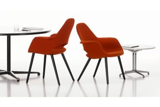 Twee rode stoelen met zwarte poten bij twee ronde tafels met witte bladen in een moderne kantooromgeving.