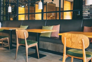 Moderne eetkamer met houten tafels, houten stoelen met groene zitting, donkergroene zitbank met gele en geruite kussens, hang