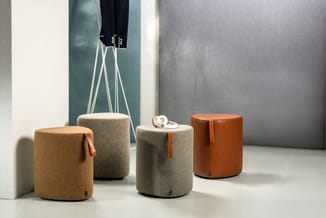 Vier cilindervormige poefs in beige, grijs en cognackleur met leren handvaten, gerangschikt in een kantoorruimte met akoestis