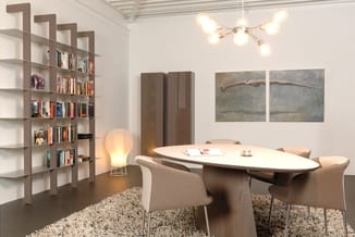 Moderne vergaderruimte met ovale witte tafel, beige stoelen, bruine boekenkast, hanglamp, wandschilderijen en grijs tapijt.