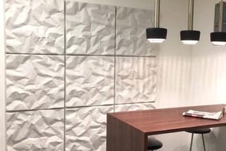 Modern kantoor met textuur akoestiekpanelen aan wand, houten bureau, zwarte hanglampjes en minimalistische inrichting.