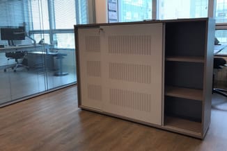 Houten kast met perforeerde schuifdeur en open legplanken, in modern kantoorinterieur met glazen wand.