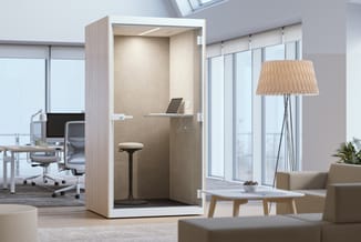 Akoestische belcel met lichte houten frame en beige binnenwanden, ingericht met laptop, staande zit-sta kruk en plafondverlic