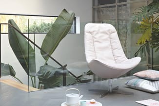 Moderne kantoorinrichting met witte loungestoel, potplanten, glazen scheidingswand en theeset op tafel bij raam.