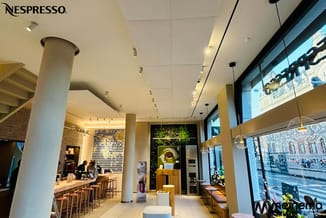 Nespresso boutique interieur met beige/gele wanden, witte plafond, wit zuilen, bar met houten krukken, glazen gevel met uitzi