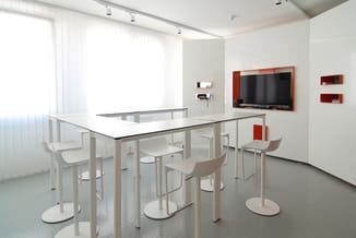Moderne vergaderruimte met rechthoekige tafel, witte stoelen, groot scherm aan rode wand, ramen met gordijnen, rode kastjes,