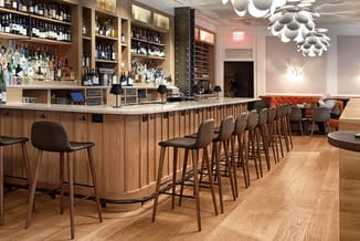 Moderne barruimte met houten bar, zwarte barkrukken, achtergrondwanden vol glazen kasten met flessen, verlichtingsarmatuur, z