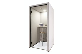 Witte belcel met grijze wanden, geopende deur, barkruk, werkblad en plafondverlichting.