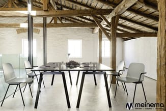 Moderne vergadertafel met zwart blad en zwarte poten, omgeven door vier grijze stoelen in een loftige ruimte met houten balke