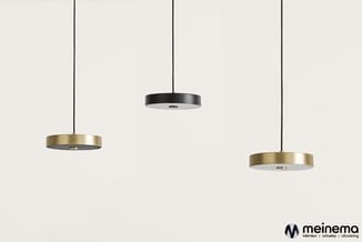 Drie hangende plafondlampen in minimalistisch design: twee met messing/goudkleurige rand en een zwarte in het midden, tegen n