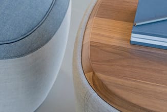 Houten ronde tafel met beige stoffen stoel en grijze fauteuil, blauwe boeken op tafelblad, detail bovenaanzicht.