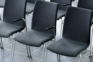 Zwarte bezoekersstoelen met gestoffeerde zitting en rugleuning, metalen frame, op een donkere vloer in een vergaderruimte.