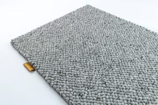 Grijze tapijttegel met gestructureerd woven oppervlak en gouden etiket, weergegeven op wit.