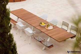 Lange houten vergadertafel met witte en geweven stoelen op terrastegels, geel fruit en drankjes op tafel.