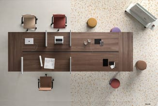Bovenaanzicht van een werkplek met bruin houten bureau, twee laptops, witte koptelefoons, drie gekleurde ergonomische stoelen