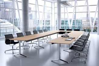 Moderne vergaderzaal met twee houten vergadertafels, zwarte bureaukstoelen, betonnen zuilen en raampartijen met uitzicht op s