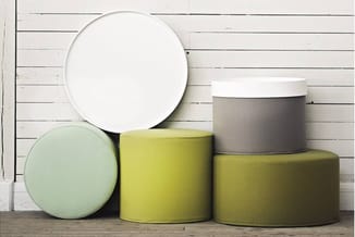 Verzameling poefs en zitobjecten in wit, mint, geel en olijfgroen met verschillende hoogtes, tegen witte houten wand.