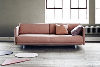 Roze-bruin linnen bank met metalen poten in minimalistisch interieur met houten vloer en grote ramen.