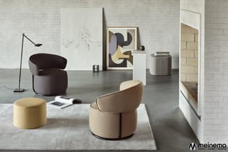 Moderne showroom met ronde stoelen in beige en donkerbruin, gele poef, zwarte vloerlamp, kunstwerken en witte kasten op beton