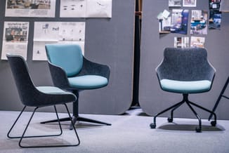 Drie moderne stoelen met donkergrijze stof en lichtblauw zitkussen, metalen onderstel, in kantooromgeving met grijze wand en