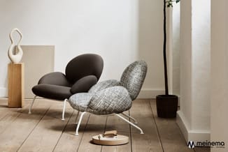 Twee organisch gevormde stoelen met witte poten in een minimalistisch interieur: één zwart, één grijs geweven, naast een potp