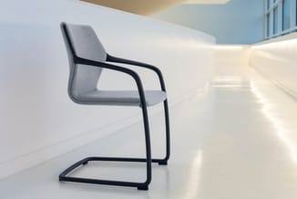 Grijze cantileverstoelmet zwart metalen frame in moderne, lichte kantoorruimte met witte wanden.