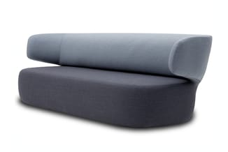 Grijze moderne sofa met gebogen vormen en ronde hoeken, voorzien van bolster-rugkussen, op witte achtergrond.