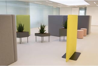 Kantoorinrichting met akoestische schermen in beige, grijs en geel, plantenbakken en roze poefjes in modern kantoor.