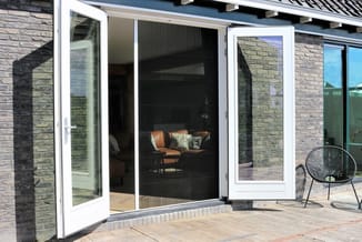 Moderne glazen schuifdeuren met wit frame en zwart gaas, open naar terras met houten vloer en tuinmeubilair.