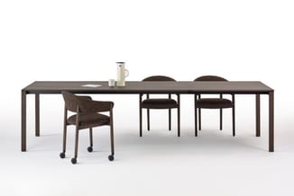 Lange donkergrijze vergadertafel met zwarte onderstel, vier bruine gestoffeerde stoelen, één stoel op wielen, minimalistische