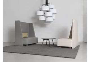 Modern kantoorinterieur met twee grijze akoestische fauteuils, zwart tafeltje, hangende witte cilinderlamp en grijze vloermat