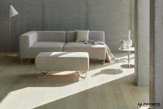 Grijze modulaire sofa met ottomaan, witte staanlamp en bijzettafel in minimalistisch interieur met betonnen wanden en houten