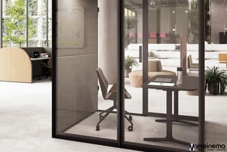 Glazen belcel met zwart frame, zwarte bureaustoel en tafel. Grijze akoestische wanden. Open kantoorruimte met planten en natu