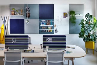 Modern kantoor met wit bureau, grijze stoelen, gestreepte bureauschermen in blauw-groen, modulaire wandpanelen en gele plant.