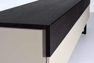 Zwarte houten vergadertafel met beige zijpaneel, detail van tafelrand en poot tegen witte achtergrond.