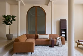 Kantoor lounge met terracotta-kleurige hoekbank, witte zuilen, ronde spiegel met houten frame, potplant, grijze vloerkleed en