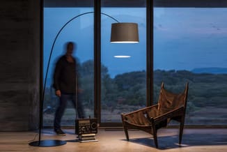 Moderne kantoorruimte met boogvloerlamp met grijze kap, bruinleren fauteuil, vintage radio en grote ramen met uitzicht op lan