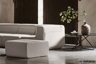 Moderne zithoek met beige/crème gekleurde modulaire bank en bijpassende poef, zwarte bijzettafel met ceramic vaas en plantdec