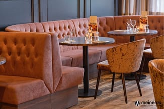 Loungeset met roze/terracotta chesterfield bank, gele/okergele fauteuils en zwarte bijzettafels in moderne hotelbar.