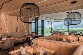 Modern restaurant interieur met houten binnenwanden, bruine lounge banken, houten tafels, zwarte hanglampkappen en glazen wan