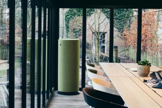 Moderne kantoorruimte met glazen wanden, houten vergadertafel, groene akoestische cilinder en ergonomische bureaustoelen met