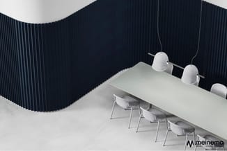Vergaderruimte met witte tafel, grijze stoelen, hangende sfeerverlichting en donkerblauwe akoestische wandpanelen.