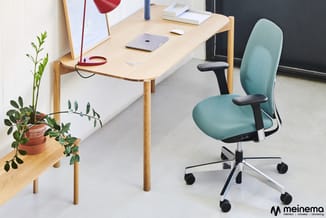 Houten bureau met afgeronde hoeken en turquoise bureaustoel met armsteunen op wielen, potplant op bijzettafel, kantoor-werkpl