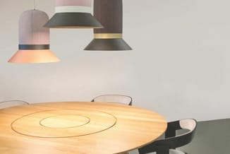 Ronde houten vergadertafel met concentrische inlegwerk en hangende designlampen in roze, zwart en grijs boven.