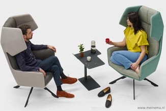 Twee personen in ergonomische fauteuils met hoge rugsteun in grijs en groen, gescheiden door een zwart bijzettafeltje met pla