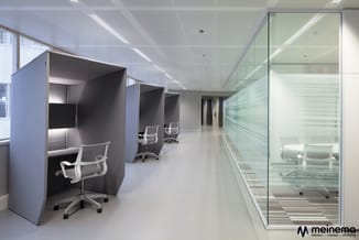 Moderne kantoorruimte met grijze akoestische belcellen, witte bureaustoel, glazen afscheiding en striped vloer.